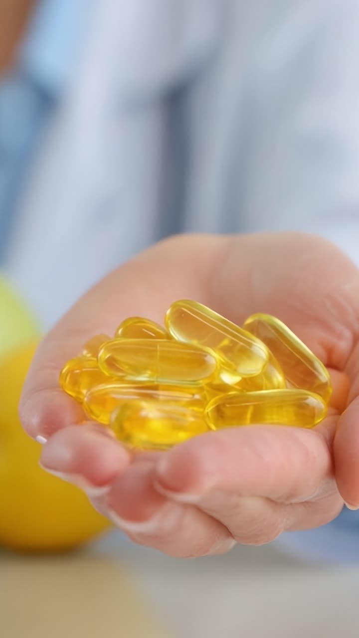 Uno sguardo ravvicinato agli integratori salutari: mano che tiene capsule di gel dorate ricche di nutrienti, colori vivaci e un impegno per il benessere e la nutrizione