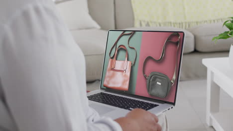 biracial woman using laptop at home online shopping for handbags, slow motion