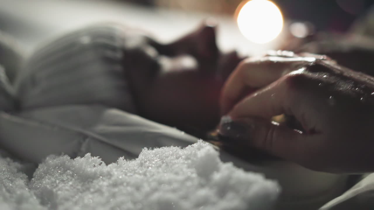 Close up of woman lying on snow at night touching her hair with wet hand, snowflakes melting under warm lights, capturing intimate peaceful moment with soft movement and emotional depth