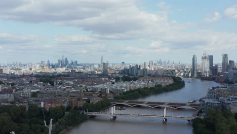 Rising-footage-over-Thames-river.-Aerial-panoramic-view-of-buildings-in-city.-Residential-district-on-river-bank-and-skyscrapers-in-business-hub-in-distance.-London,-UK