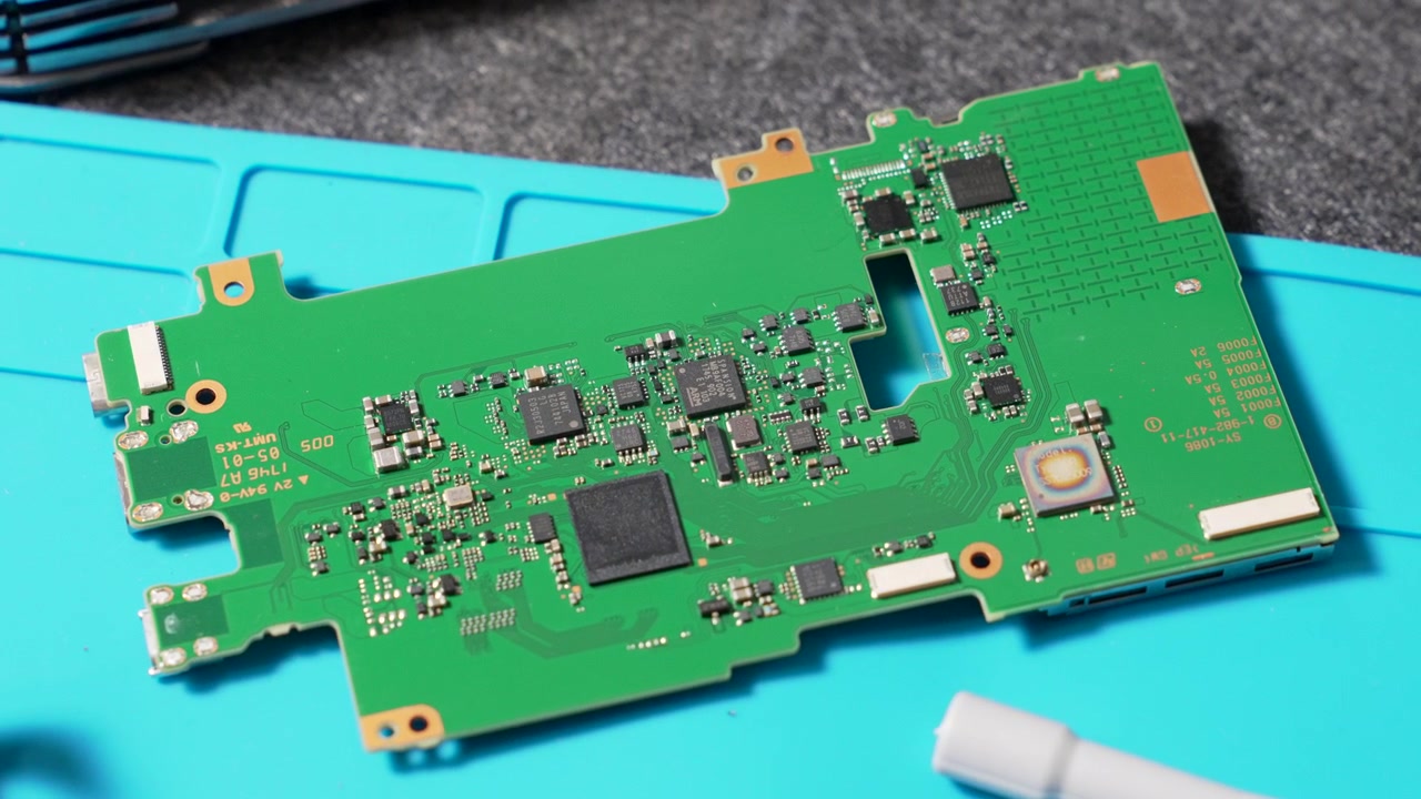 Camera motherboard featuring intricate circuit board design and various integrated electronic components placed on a blue work mat.