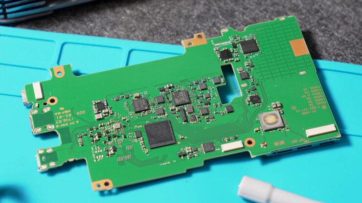 Kameramoderkort med indviklet printpladedesign og forskellige integrerede elektroniske komponenter placeret på en blå arbejdsunderlag.