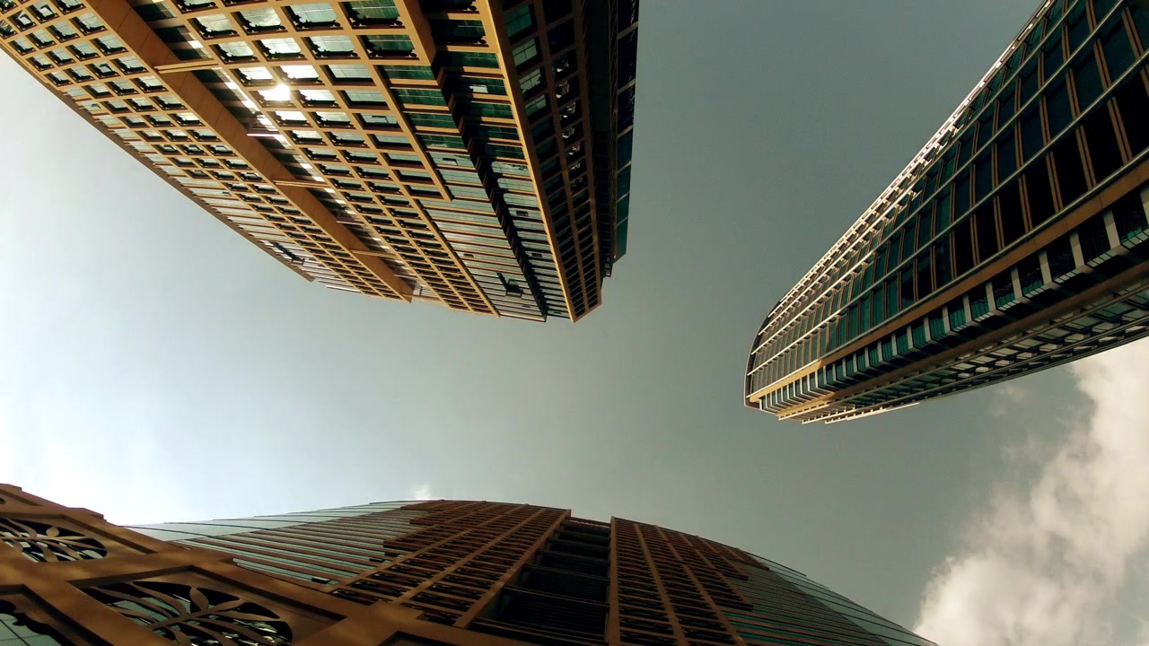 La telecamera punta dritto verso l'alto mentre tre grattacieli convergono verso un cielo nuvoloso ad Abu Dhabi, vista dal basso.