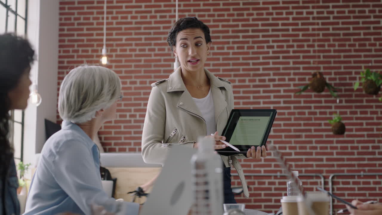 사업가들이 모여 브레인스토밍을 하고 히스패닉 팀 리더 여성이 스타트업 프로젝트에 대한 창의적인 아이디어를 공유하고 태블릿 컴퓨터를 사용하여 전략을 제시하고 현대 사무실 프레젠테이션에서 동료를 훈련시 ⁇ 니다.