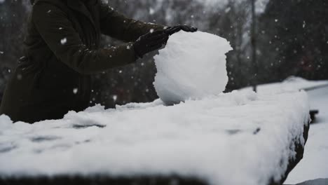 chica hace muñeco de nieve en la mesa de picnic mientras cae la nieve, cámara lenta