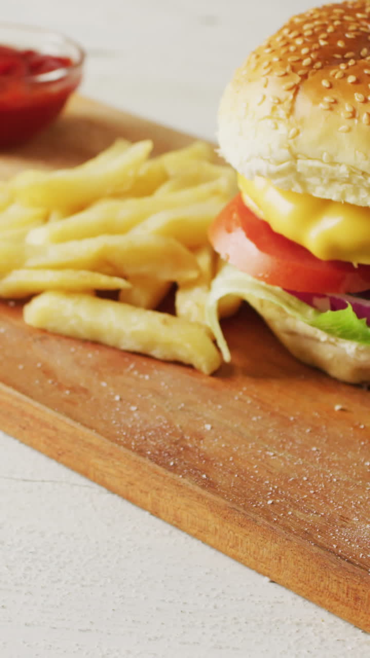video de una hamburguesa con queso, papas fritas y un cuenco de ketchup en una tabla de madera