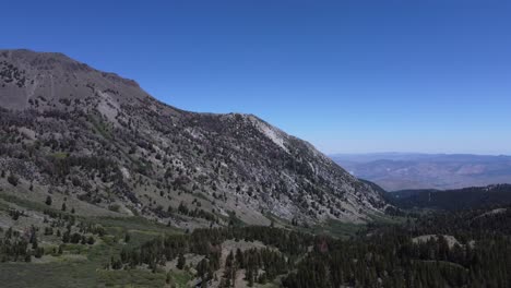 Aerial-shot-of-a-mountain-towering-over-a-forested,-green-valley-in-Northern-Nevada