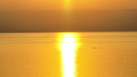 friends paddleboard in the ocean during sunrise with mountains in the background