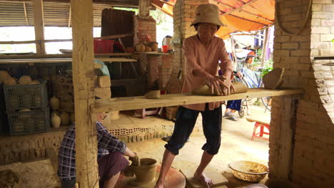 un alfarero asiático experto trabaja en arcilla nueva mientras que otra mujer da forma a la cerámica en una mesa giratoria, mostrando el arte y la artesanía de la cerámica tradicional