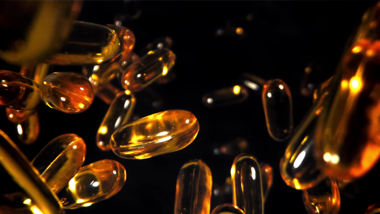 Capsule vitaminiche dorate in caduta al rallentatore su sfondo nero