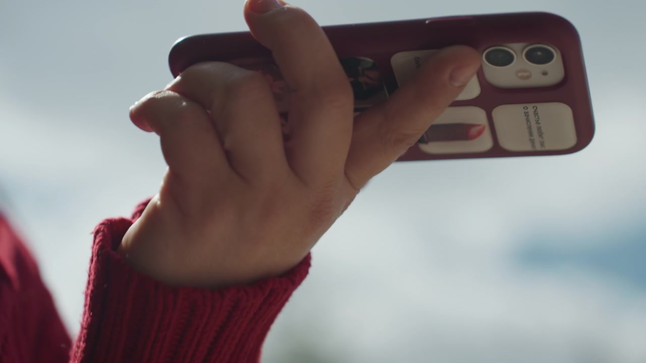 Close up of woman hand holding and interacting with smartphone wearing red knitwear. focus remains on fingers gripping or tapping device throughout emphasizing human device interaction