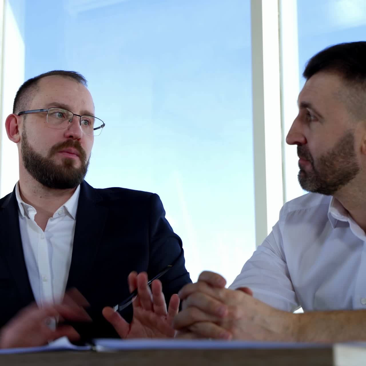 Portrait of two businessmen talking in office. Serious partners discussing business strategy indoors on window background at daytime. Business concept
