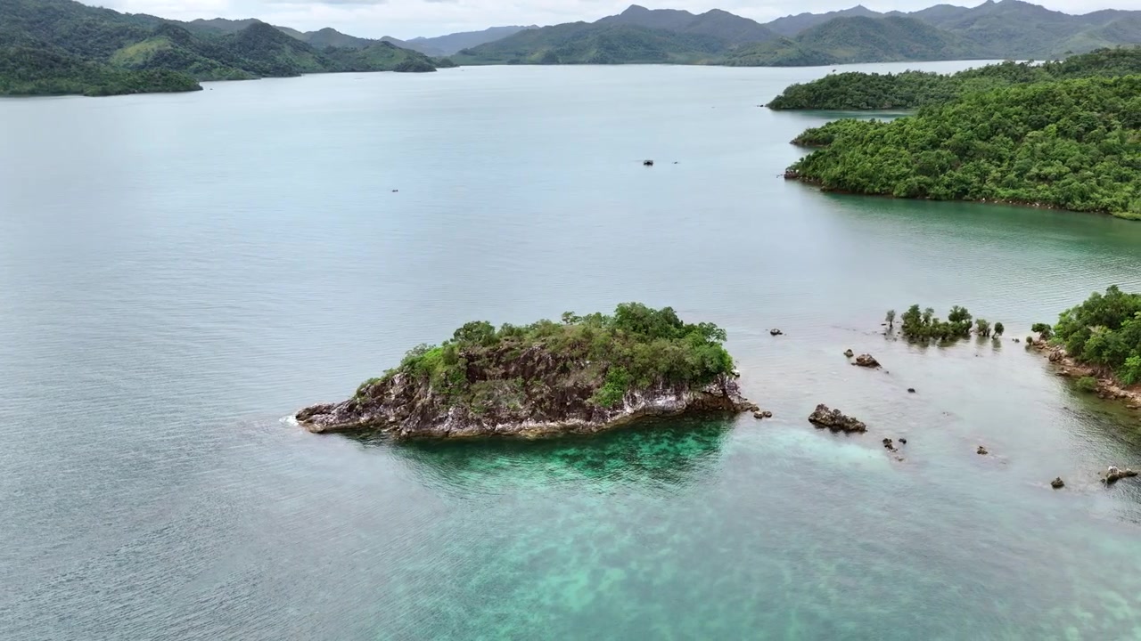 Rekaman drone orbit sebuah pulau kecil dekat pesisir berbatu Palawan, Filipina. Pemandangan ini menangkap laut yang tenang, medan tropis, dan langit berawan yang murung, menyoroti keindahan terpencil dan pemandangan yang menawan.