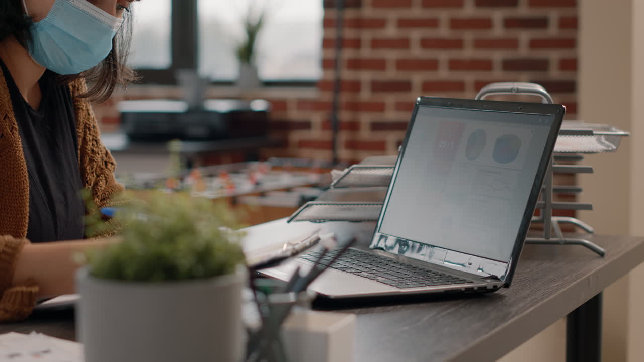 Woman in mask working on laptop in office