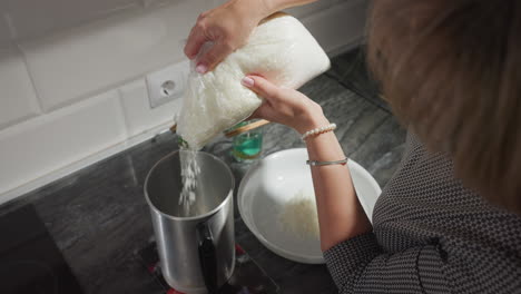 top down view female baker pouring corn flour from plastic bag into metal pot in modern kitchen setting with white plate of corn flour, green substance in glasses, chopsticks resting on glass tops