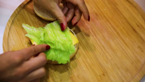 Mujer-Morena-En-Cámara-Lenta-Con-Esmalte-De-Uñas-Rojo-Está-Preparando-Una-Hamburguesa-Doble-Con-Queso-En-La-Cocina