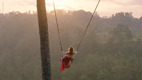 travel woman swinging over tropical rainforest at sunrise female tourist sitting on swing with scenic view enjoying freedom on vacation having fun holiday lifestyle slow motion