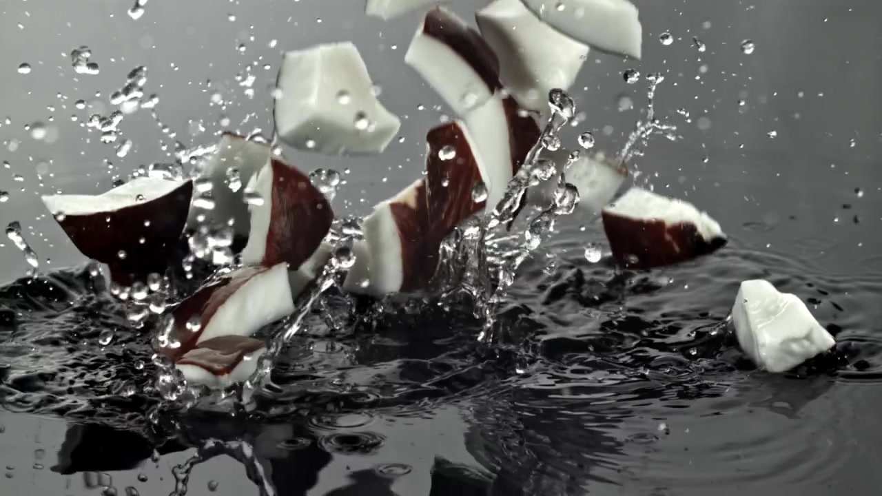 Fresh Coconut Pieces Dropping into Water with Splashes in Slow Motion