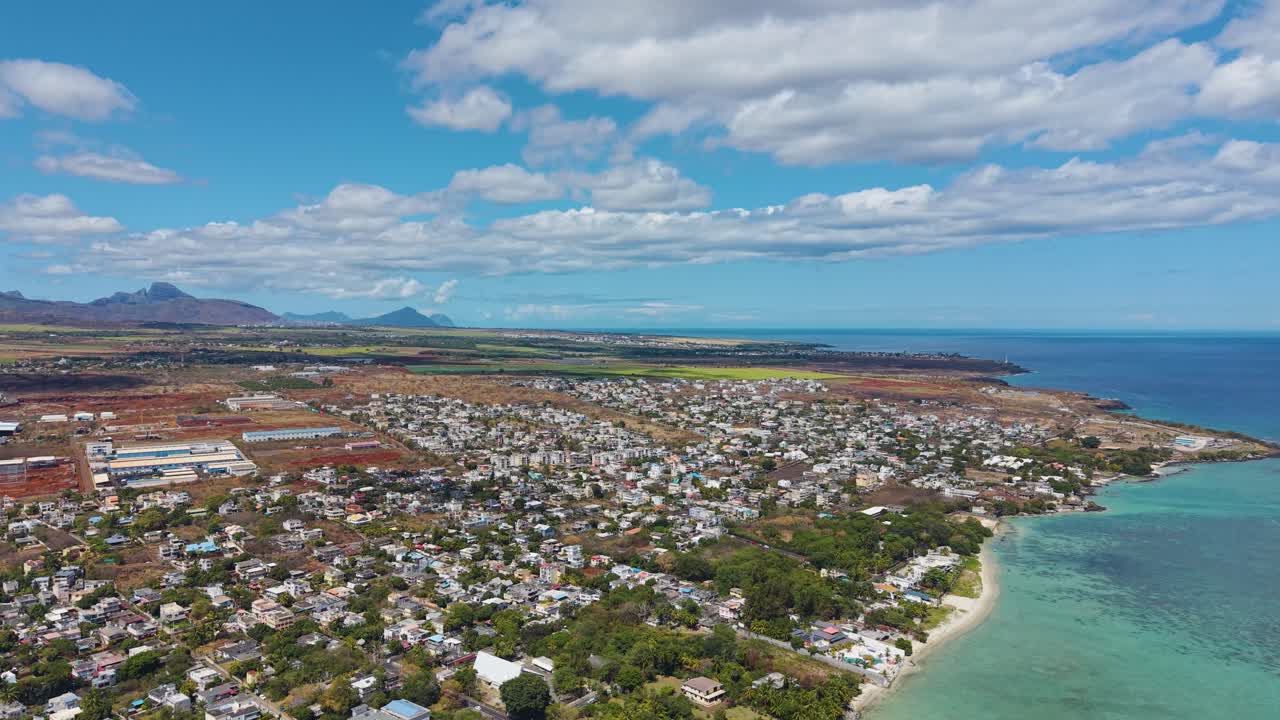 Expansive aerial view of Mauritius revealing lush fields, coastal towns, and the deep blue Indian Ocean beneath a clear sky. A serene and vibrant panorama showcasing the island’s natural beauty