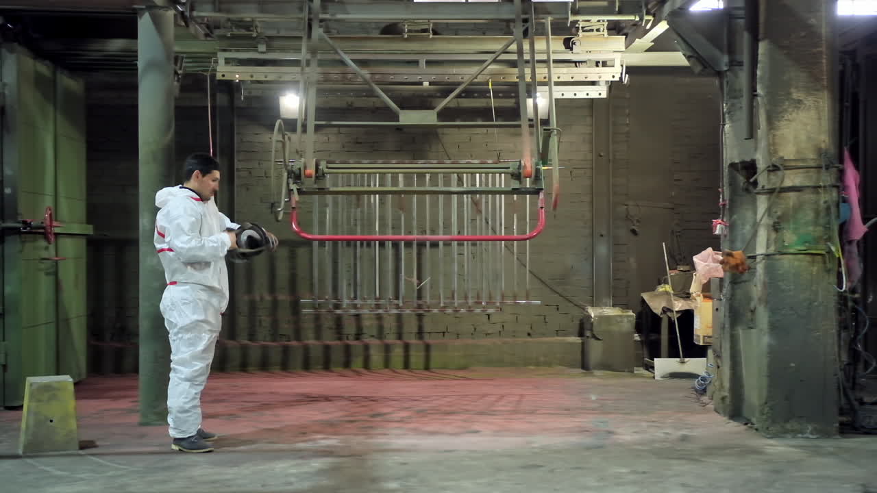 Technician starts his work inside the workshop. Worker in white protective suit putting on respirator on his head before the painting procedure.