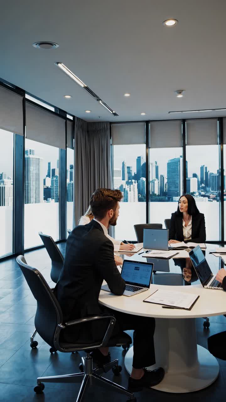 High-angle video shot of a modern office meeting with professionals in suits, laptops open