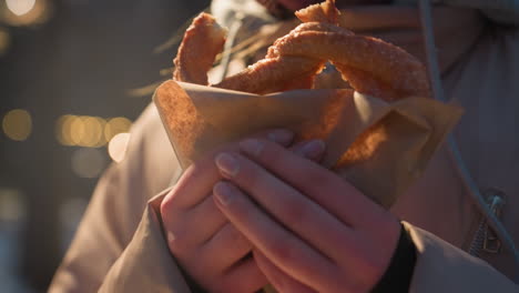 primer plano de una persona sosteniendo un delicioso bocadillo en la mano, iluminado por una luz suave, mostrando giros dorados de pasteles envueltos en papel en un parque de invierno al aire libre