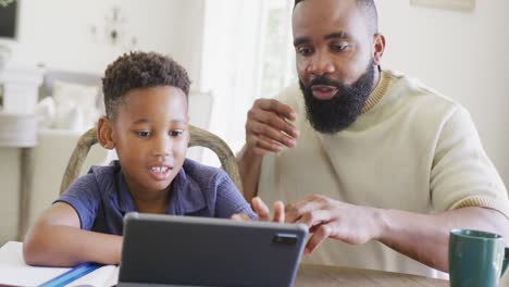 Glücklicher-Afroamerikanischer-Vater-Und-Sohn-Sitzen-Am-Tisch-Und-Machen-Gemeinsam-Hausaufgaben,-In-Zeitlupe