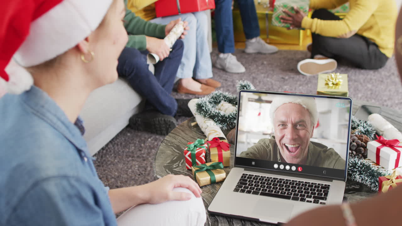 amigos diversos con sombreros de santa teniendo una llamada de video portátil con un hombre caucásico feliz