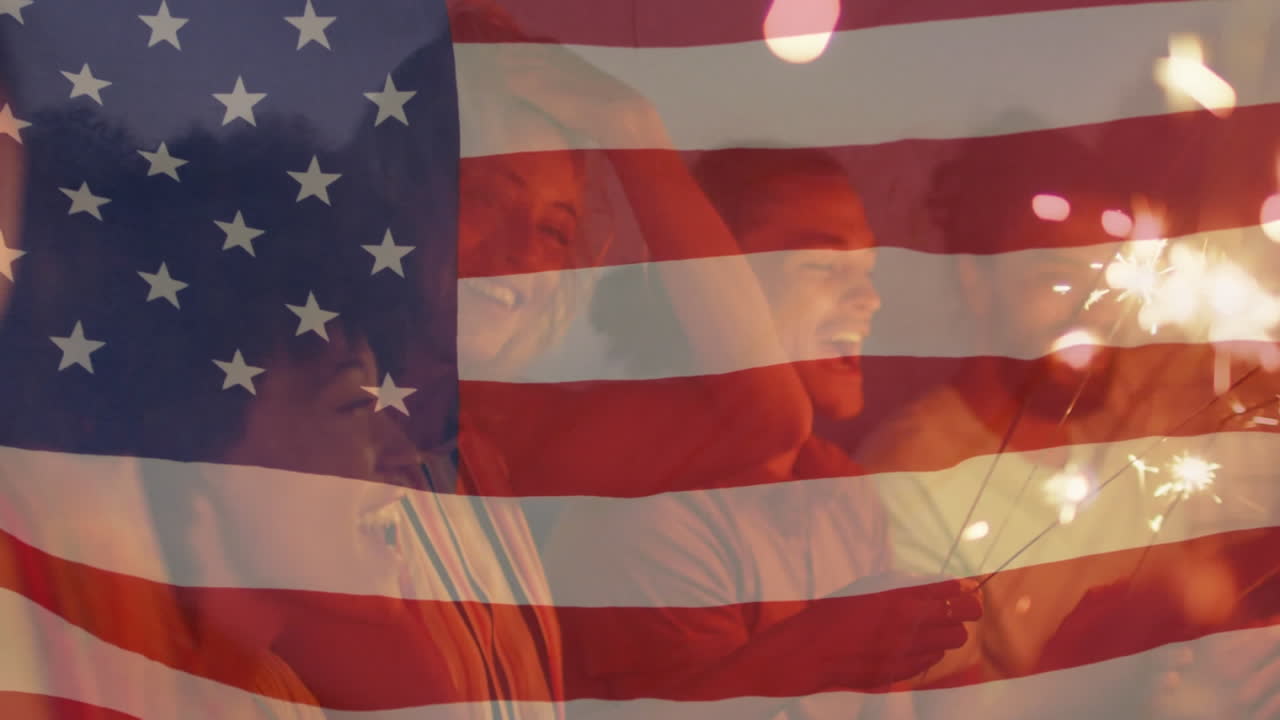 animación de la bandera estadounidense ondeando sobre un grupo de amigos que sostienen chispas en la playa