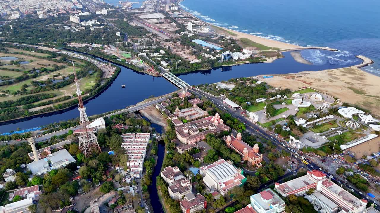 Vista aerea cinematografica di Chennai dei Memoriali Anna e Kalaignar accanto ai Memoriali MGR e Jayalalithaa — archi iconici e giardini paesaggistici sullo sfondo di Marina Beach e del Golfo del Bengala.