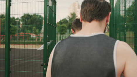 two male basketball players walking together and talking each other, while entering in an outdoor basketball court