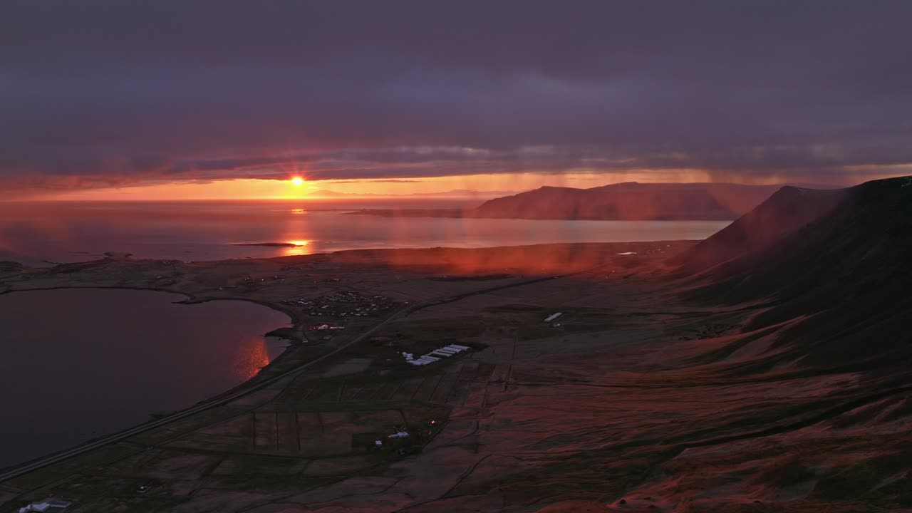 A vibrant sunset paints the sky in fiery hues over Akranes, Iceland, casting a warm glow across the coastal landscape and waters