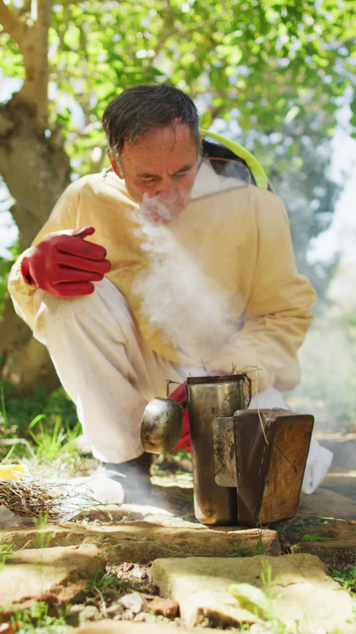 보호복을 입고 흡연자를 준비하는 고위 백인 수 양봉업자의 수직