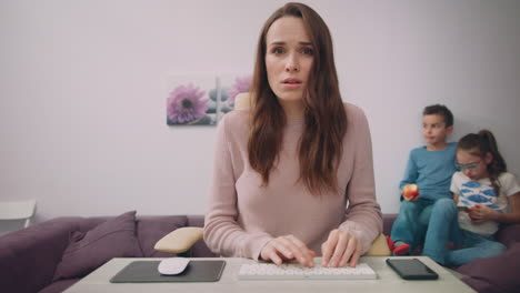 madre trabajando en la computadora en casa con los niños jugando en el fondo