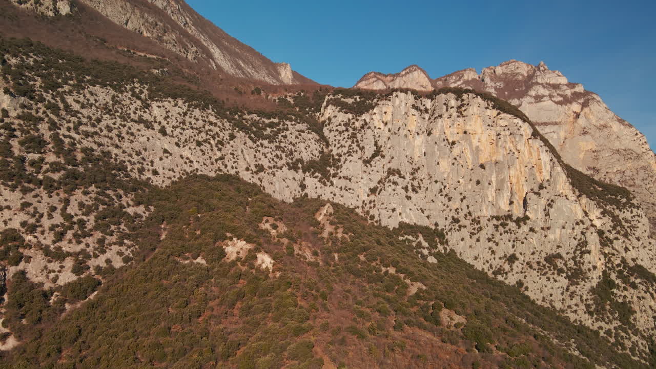 이탈리아 북동부 트렌티노의 푸른 맑은 하늘을 배경으로 초목이 있는 석회암 산 가까이 날아갑니다.