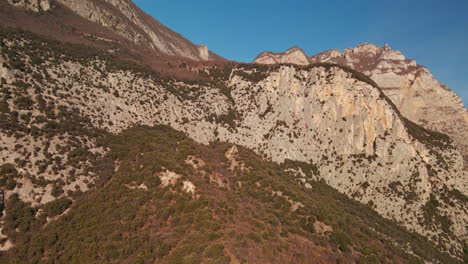 flying close to limestone mountains with vegetations against blue clear sky in trentino, northeastern italy