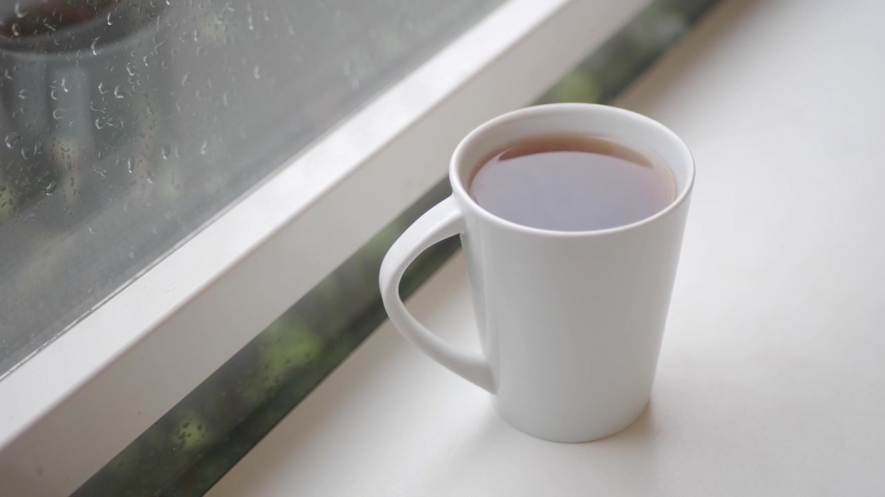 White Mug of Tea on a Windowsill with Raindrops