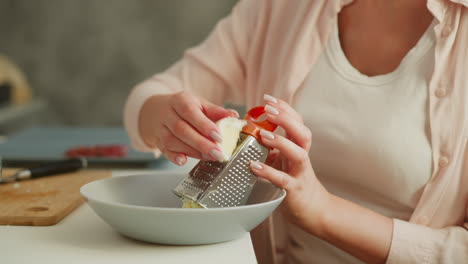 culinary artist skillfully grating boiled egg using metal grater into bowl, focusing on careful hand placement to avoid injury during food preparation on clean kitchen table