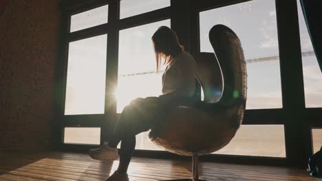 Female-model-sit-on-retro-vintage-aviator-egg-chair-near-bright-wide-window