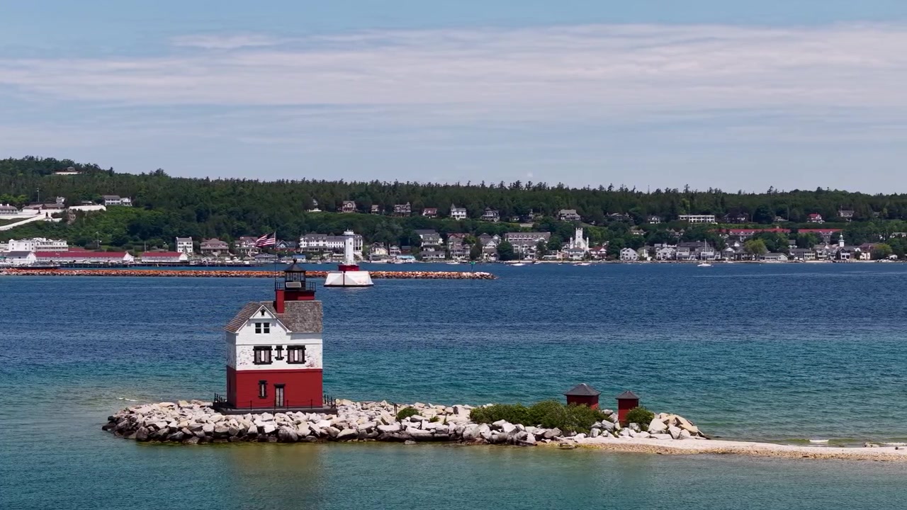 Veduta aerea del faro di Round Island su una diga frangiflutti rocciosa con acqua del lago colorata e la costa di Hessel, Michigan, sullo sfondo