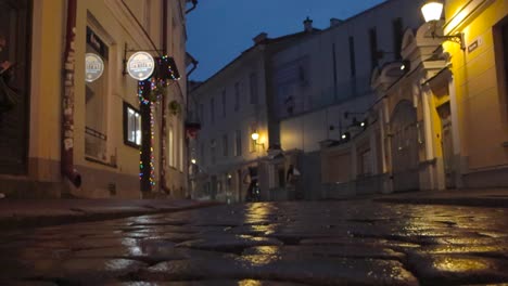 tallinn old town medieval cobblestone street filmed from a low angle or from the ground when the ground is wet and reflective. people walking in the background and filmed during night or dusk time.