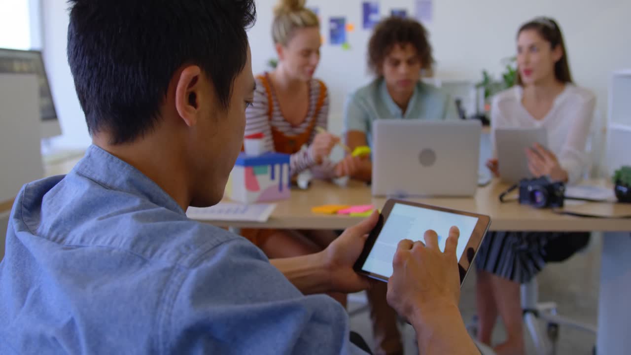 vista trasera de un joven hombre asiático trabajando en una tableta digital en una oficina moderna 4k