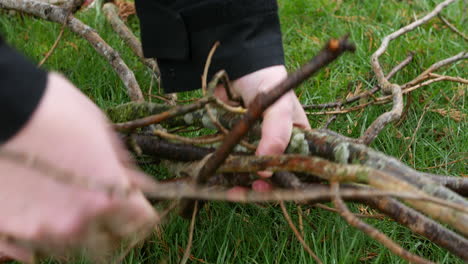 close up of a man picking up sticks and branches from the grass in a back yard field garden