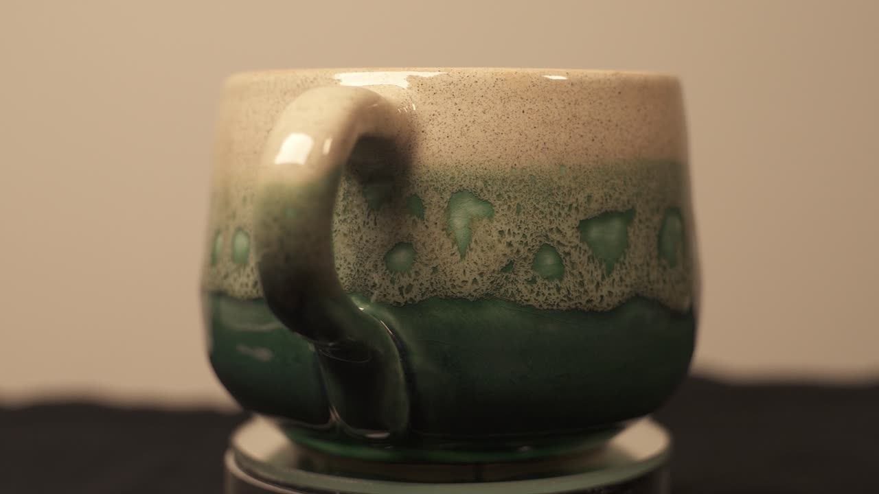 primer plano de una taza verde de cerámica casera que se muestra en una plataforma giratoria