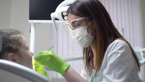 Friendly-female-dentist-examines-teeth-of-a-cute-little-girl-using-her-instruments.-Shot-in-4k