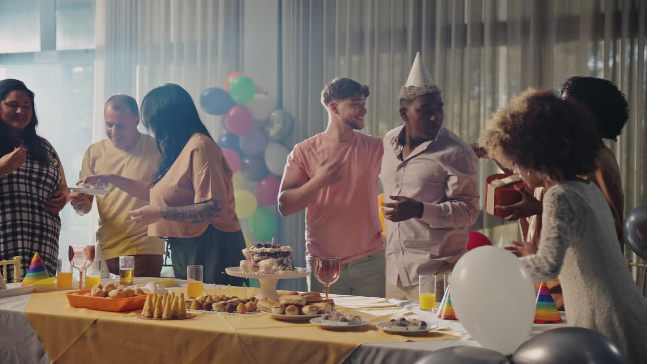 Friends and family celebrating at a lively party with food, drinks, and balloons