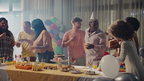 friends and family celebrating at a lively party with food, drinks, and balloons