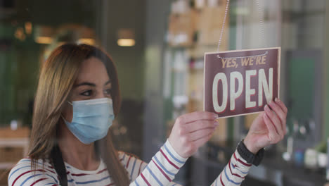 female hairdresser wearing face mask changing sign board closed to open at hair salon