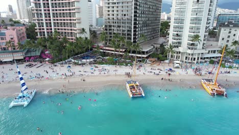 A-drone-starts-close-in-on-an-island-tropical-beach-as-families-enjoy-their-vacation-and-couples-load-onto-boats-for-a-sunset-dinner-cruise