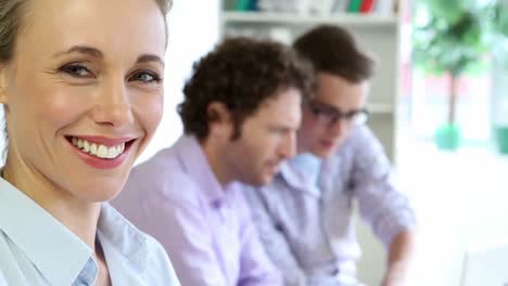 mujer de negocios sonriendo a la cámara mientras sus colegas están hablando